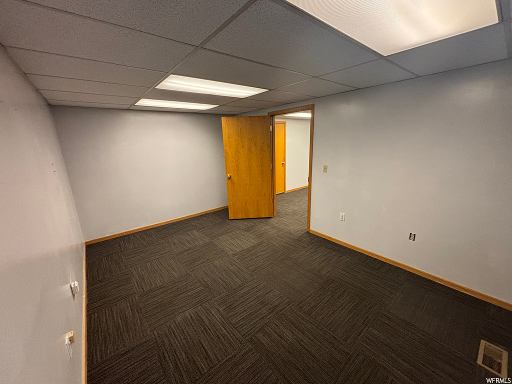 Basement with dark colored carpet and a paneled ceiling