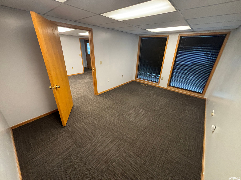 Empty room featuring dark colored carpet and a drop ceiling