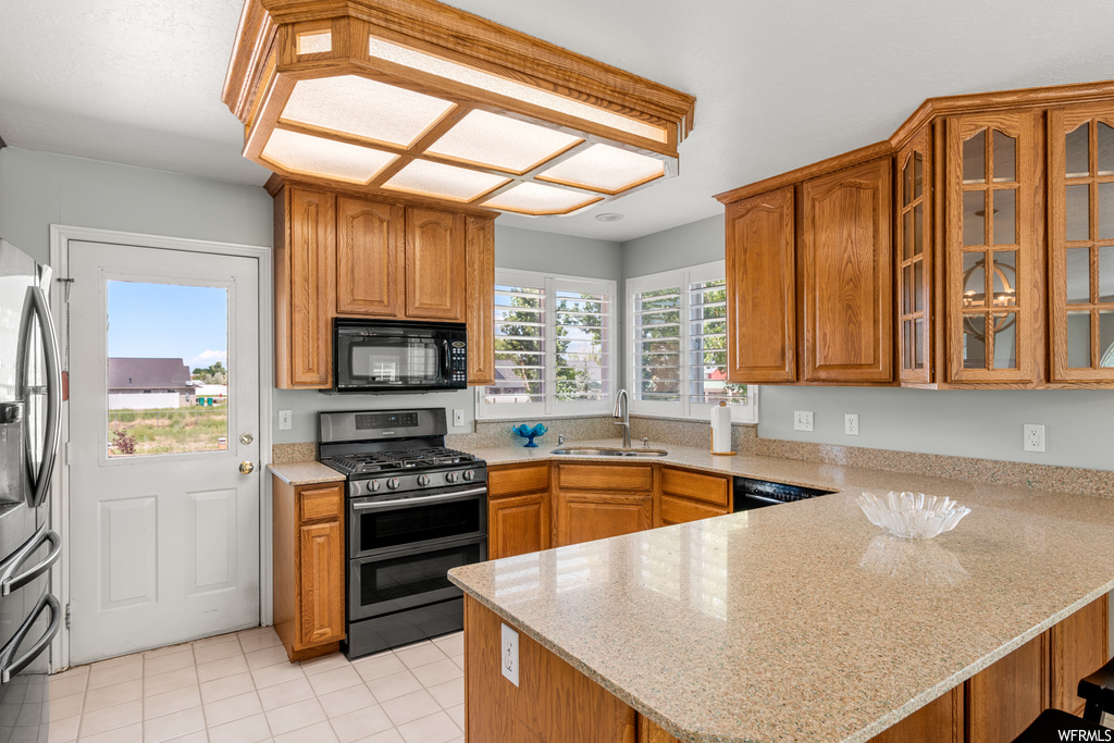 Kitchen featuring light tile flooring, stainless steel appliances, light countertops, and brown cabinets