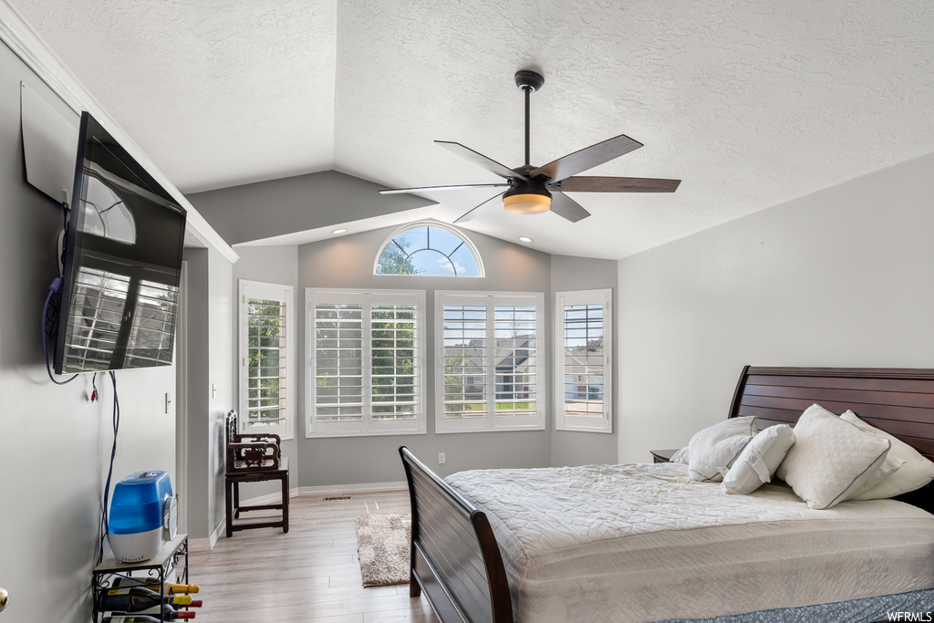 Hardwood floored bedroom with multiple windows, a textured ceiling, vaulted ceiling, and ceiling fan
