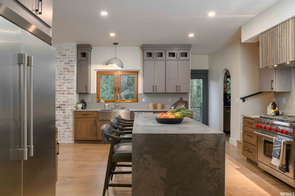 Kitchen featuring light hardwood floors, premium appliances, a center island, pendant lighting, brick wall, and light countertops