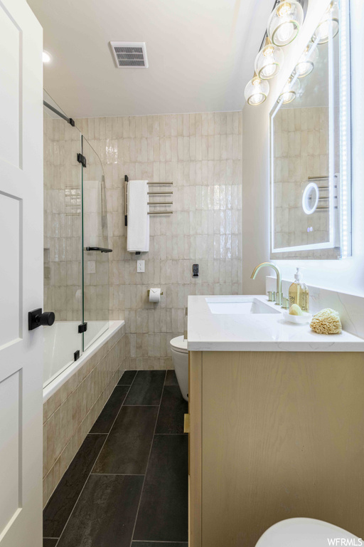 Full bathroom with tile flooring, tile walls, combined bath / shower with glass door, vanity, and mirror