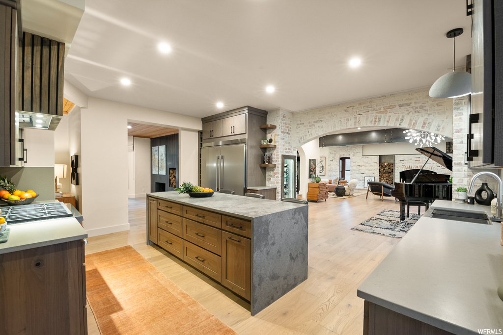 Kitchen with stainless steel built in fridge, a center island with sink, hanging light fixtures, light countertops, and light parquet floors