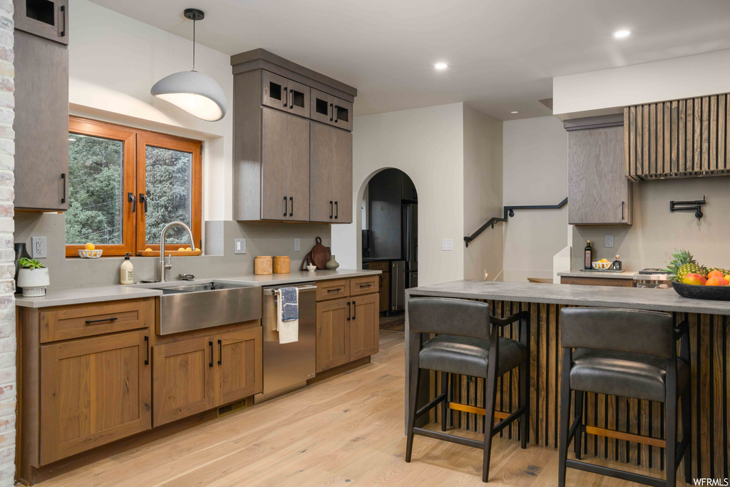 Kitchen with decorative light fixtures, brown cabinets, light hardwood flooring, a center island, stainless steel dishwasher, and light countertops