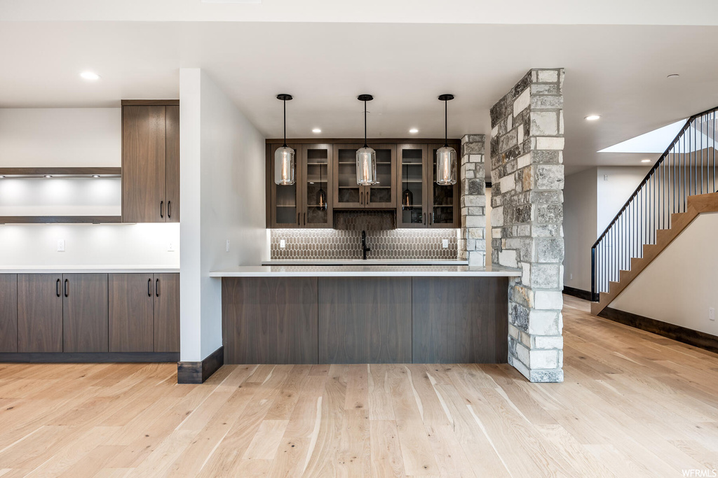 Kitchen featuring backsplash, light countertops, light hardwood floors, dark brown cabinetry, and pendant lighting