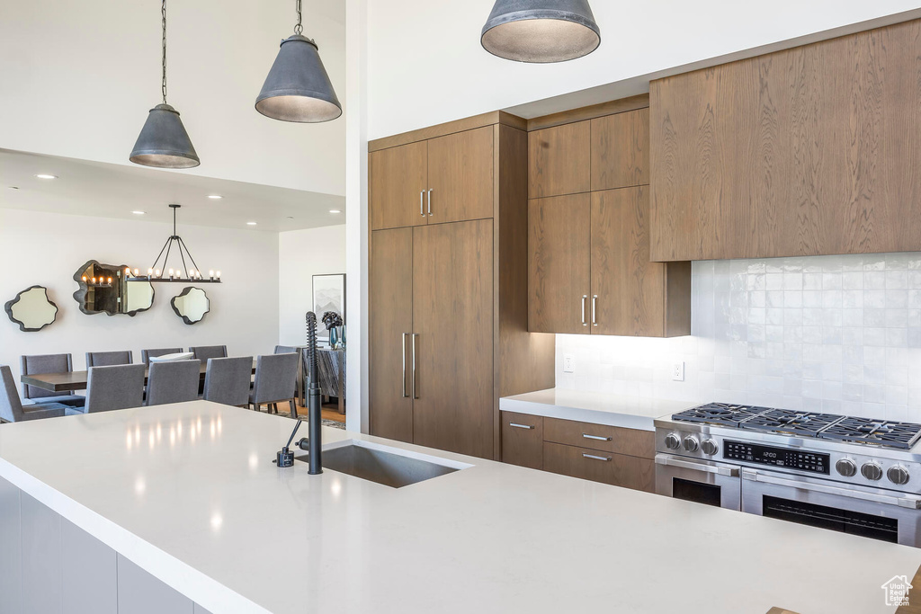 Kitchen featuring hanging light fixtures, range with two ovens, sink, and tasteful backsplash