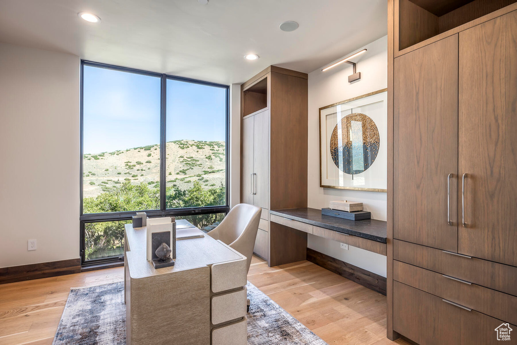 Office space featuring floor to ceiling windows, a mountain view, and light wood-type flooring