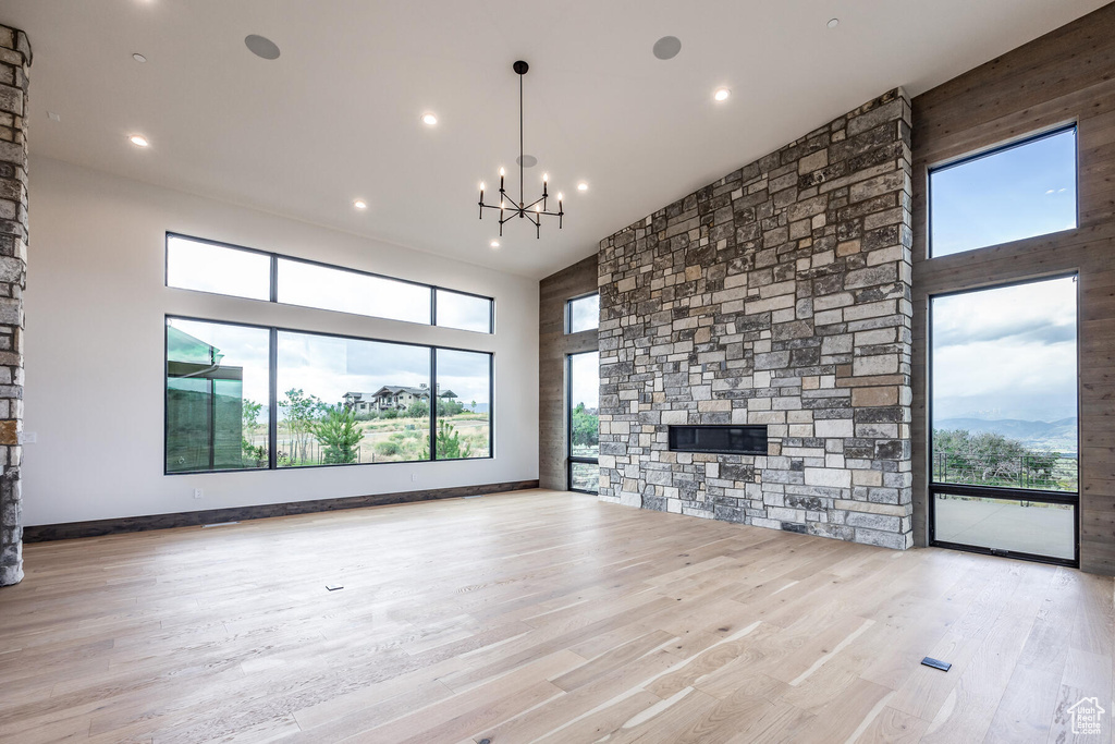 Unfurnished living room featuring high vaulted ceiling, an inviting chandelier, a fireplace, and light hardwood / wood-style floors