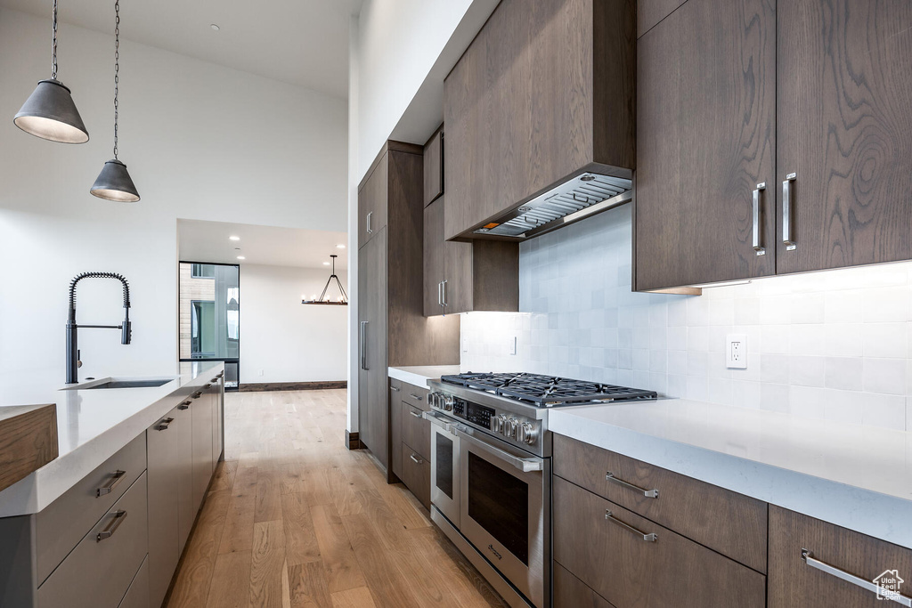 Kitchen with hanging light fixtures, range with two ovens, sink, and light hardwood / wood-style flooring