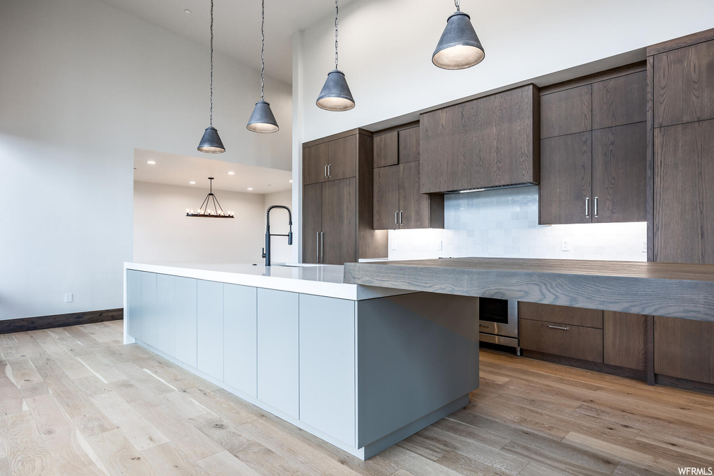 Kitchen featuring backsplash, light countertops, light hardwood flooring, pendant lighting, and a high ceiling