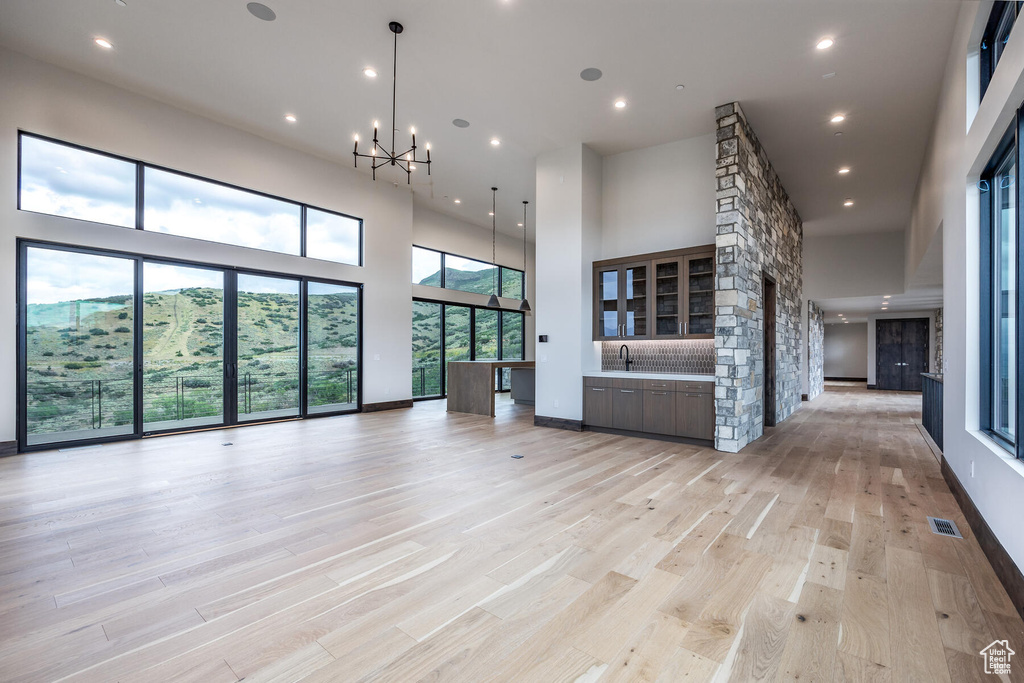 Unfurnished living room with a high ceiling, sink, an inviting chandelier, and light hardwood / wood-style flooring