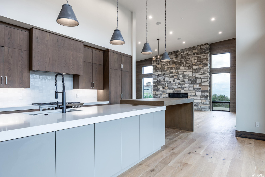 Kitchen featuring decorative light fixtures, backsplash, light countertops, light hardwood flooring, and stainless steel gas stovetop