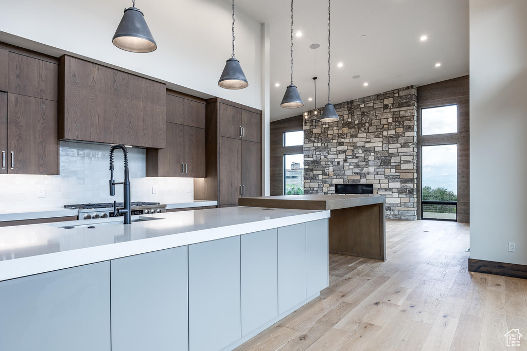 Kitchen with decorative light fixtures, a fireplace, light hardwood / wood-style flooring, backsplash, and dark brown cabinetry