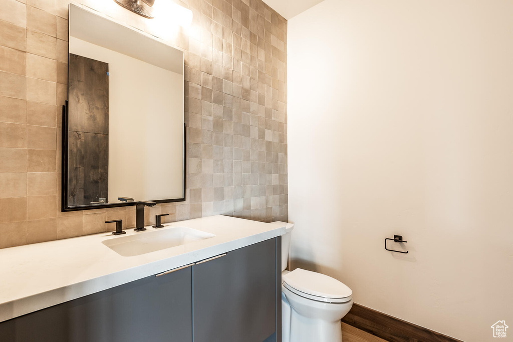 Bathroom with vanity, backsplash, wood-type flooring, tile walls, and toilet