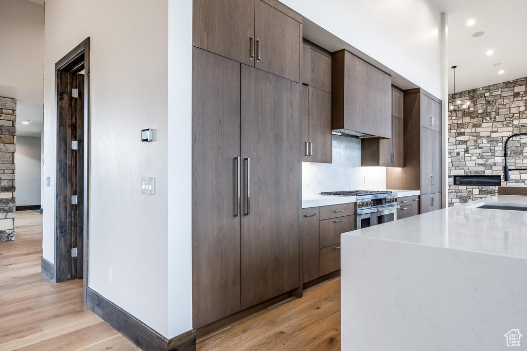 Kitchen with stainless steel range, backsplash, light hardwood / wood-style floors, hanging light fixtures, and sink