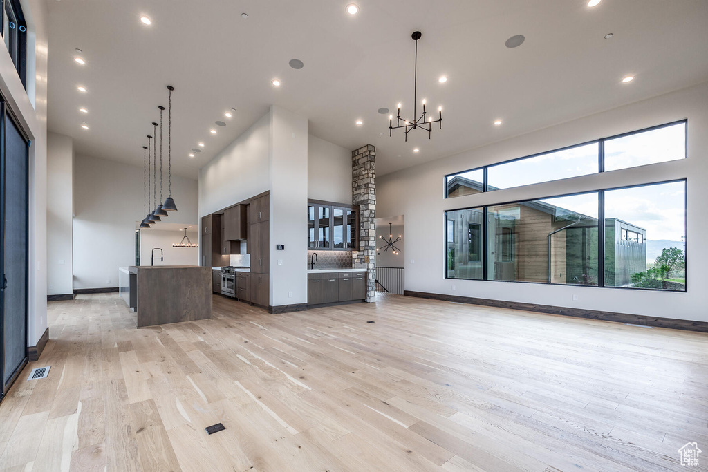 Unfurnished living room with light wood-type flooring, sink, an inviting chandelier, and a towering ceiling