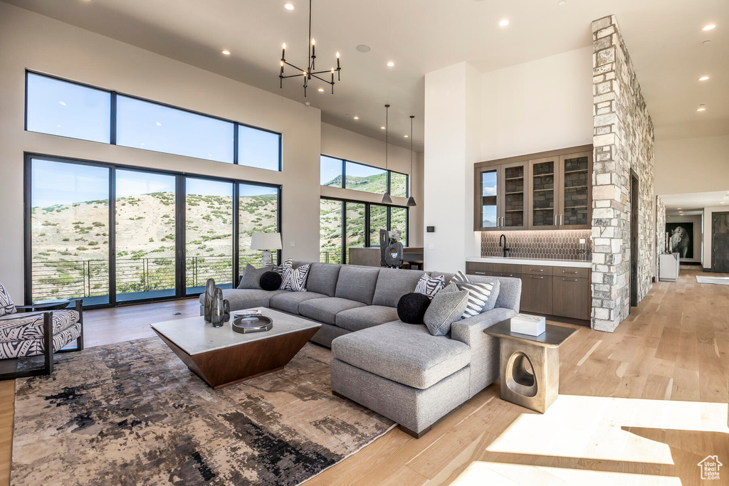 Living room featuring a high ceiling, sink, light wood-type flooring, and a chandelier