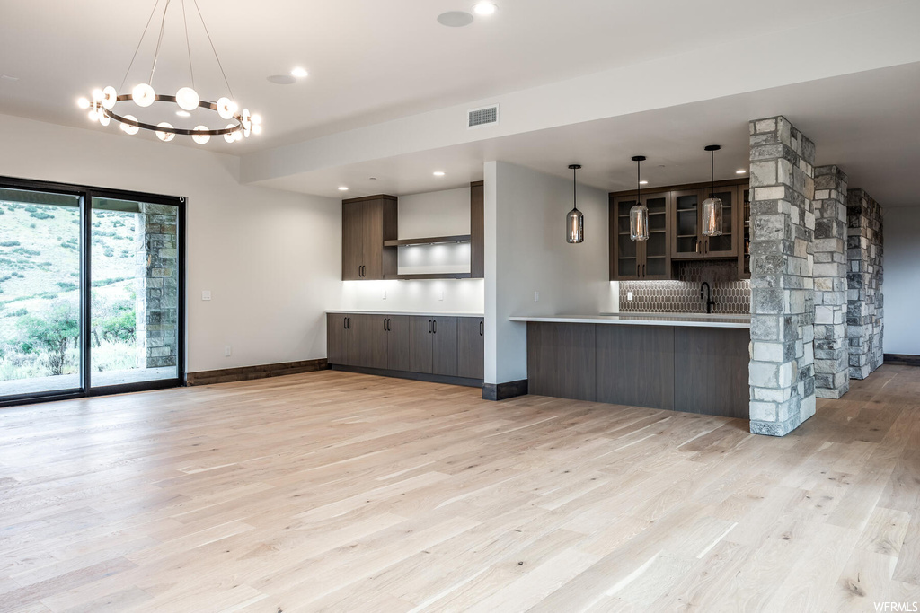 Kitchen with backsplash, light hardwood floors, dark brown cabinets, and pendant lighting