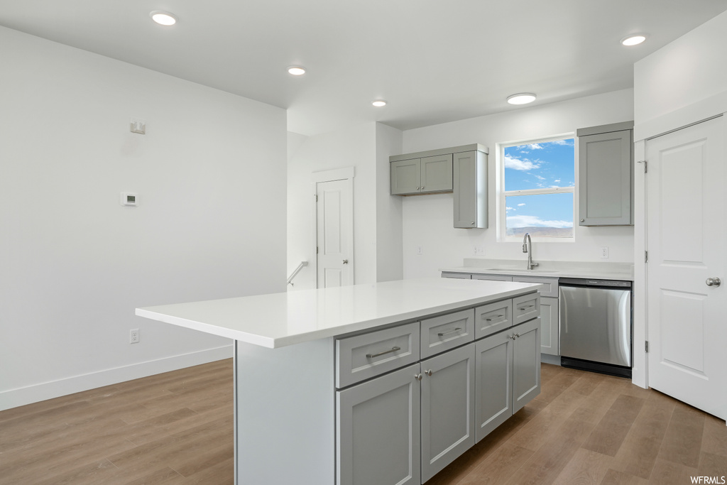 Kitchen with light countertops, stainless steel dishwasher, light hardwood floors, and white cabinets