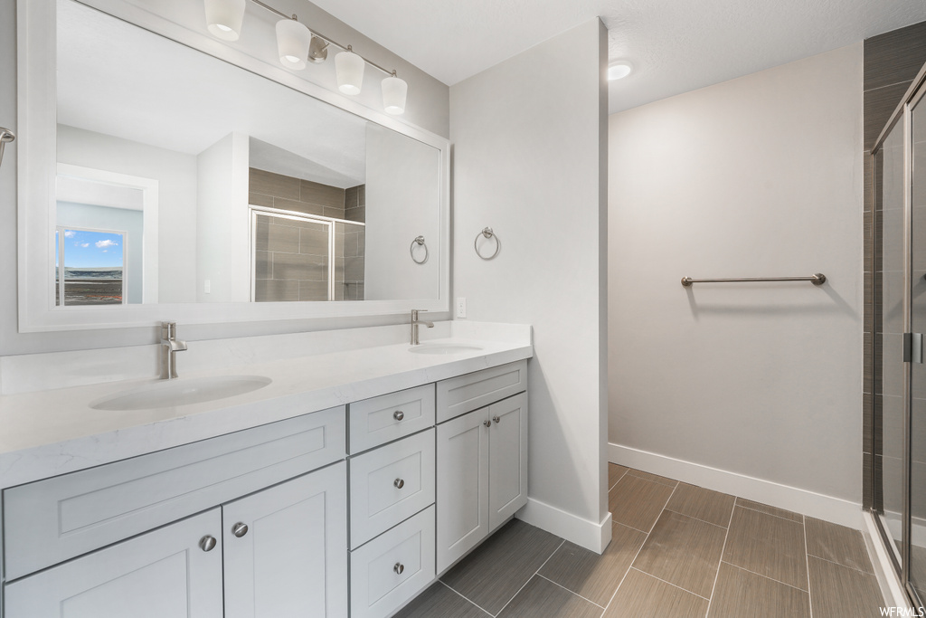 Bathroom with an enclosed shower, dual vanity, tile floors, and mirror