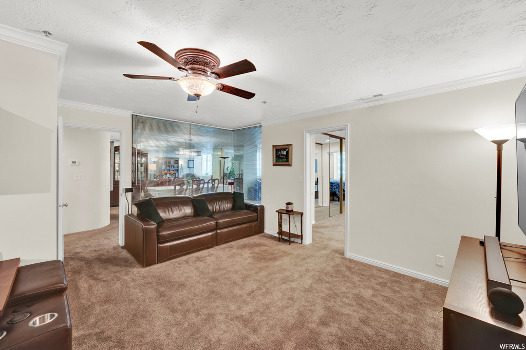 Living room featuring light carpet, a textured ceiling, ornamental molding, and ceiling fan