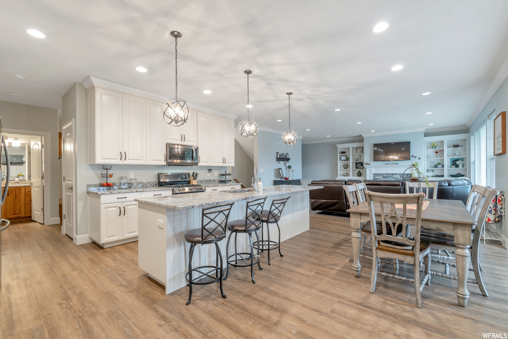 Kitchen with white cabinets, crown molding, built in features, decorative light fixtures, range, light hardwood flooring, light stone counters, and a kitchen island