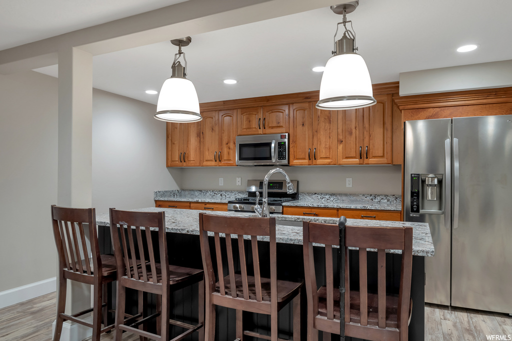Kitchen with light hardwood floors, a center island, light stone counters, hanging light fixtures, and appliances with stainless steel finishes