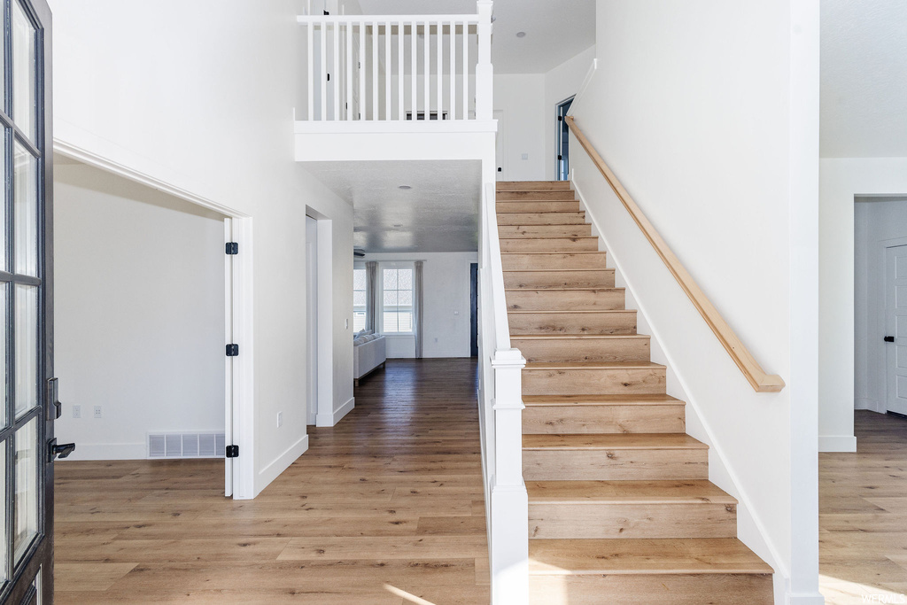 Stairs featuring a towering ceiling and light hardwood floors