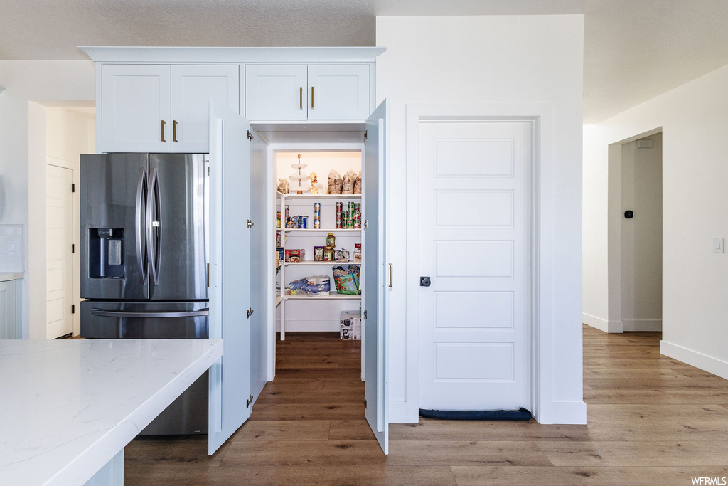 Kitchen featuring white cabinets, stainless steel fridge, light stone countertops, and light hardwood flooring