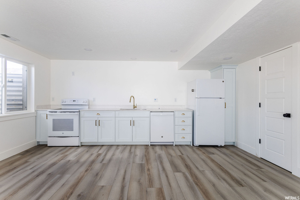 Kitchen with white appliances, white cabinetry, and light hardwood floors