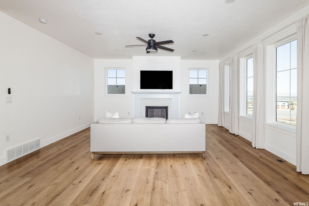 Unfurnished living room with ceiling fan, a fireplace, and light hardwood flooring