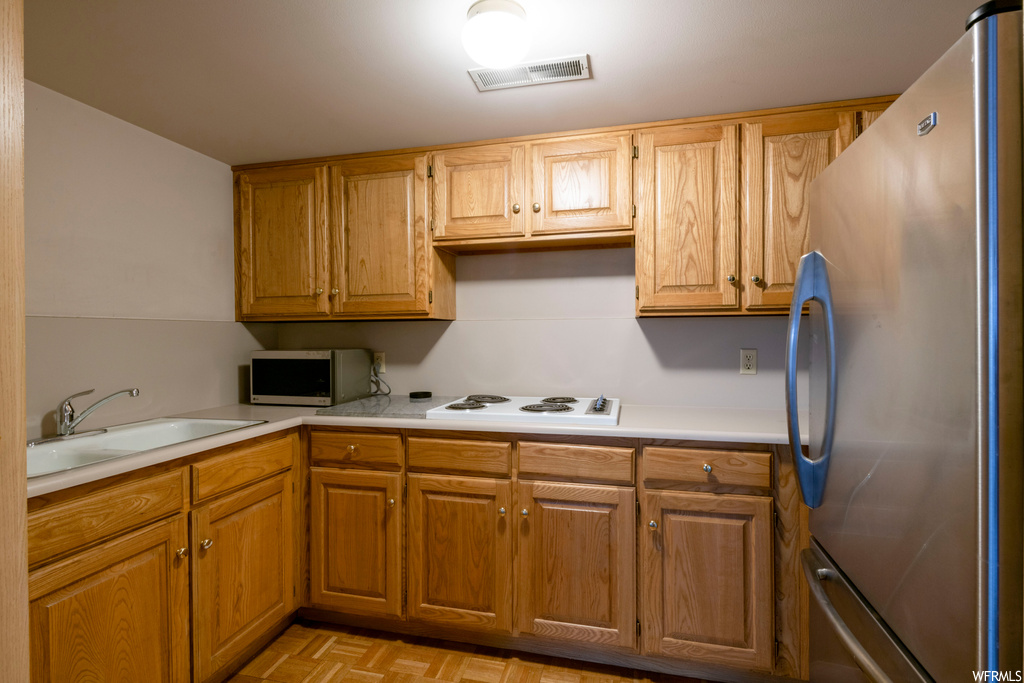 Kitchen with light countertops, brown cabinets, light parquet floors, and appliances with stainless steel finishes