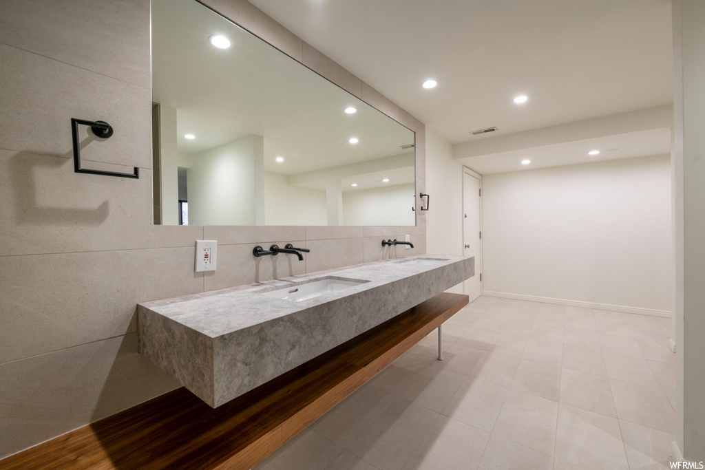 Bathroom with light tile floors, mirror, double vanity, and backsplash