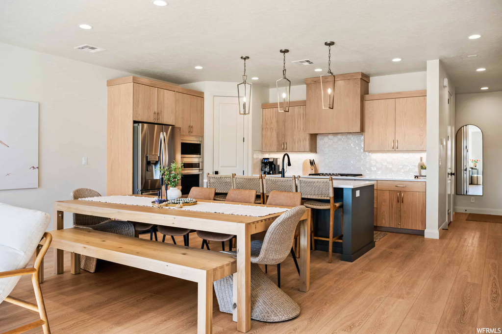 Kitchen with stainless steel appliances, decorative light fixtures, light countertops, backsplash, and light hardwood floors