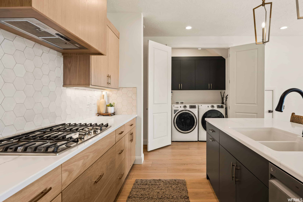 Kitchen with backsplash, wall chimney range hood, light countertops, light hardwood floors, independent washer and dryer, and stainless steel appliances