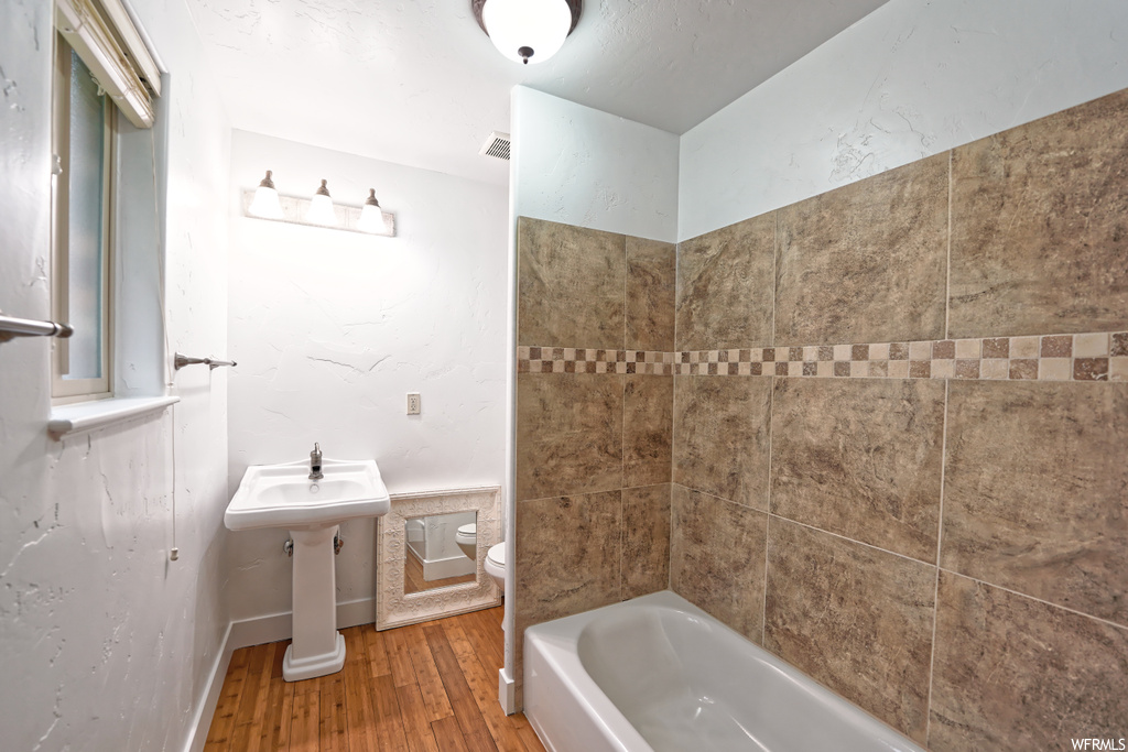 Full bathroom featuring tiled shower / bath, toilet, hardwood / wood-style floors, and sink