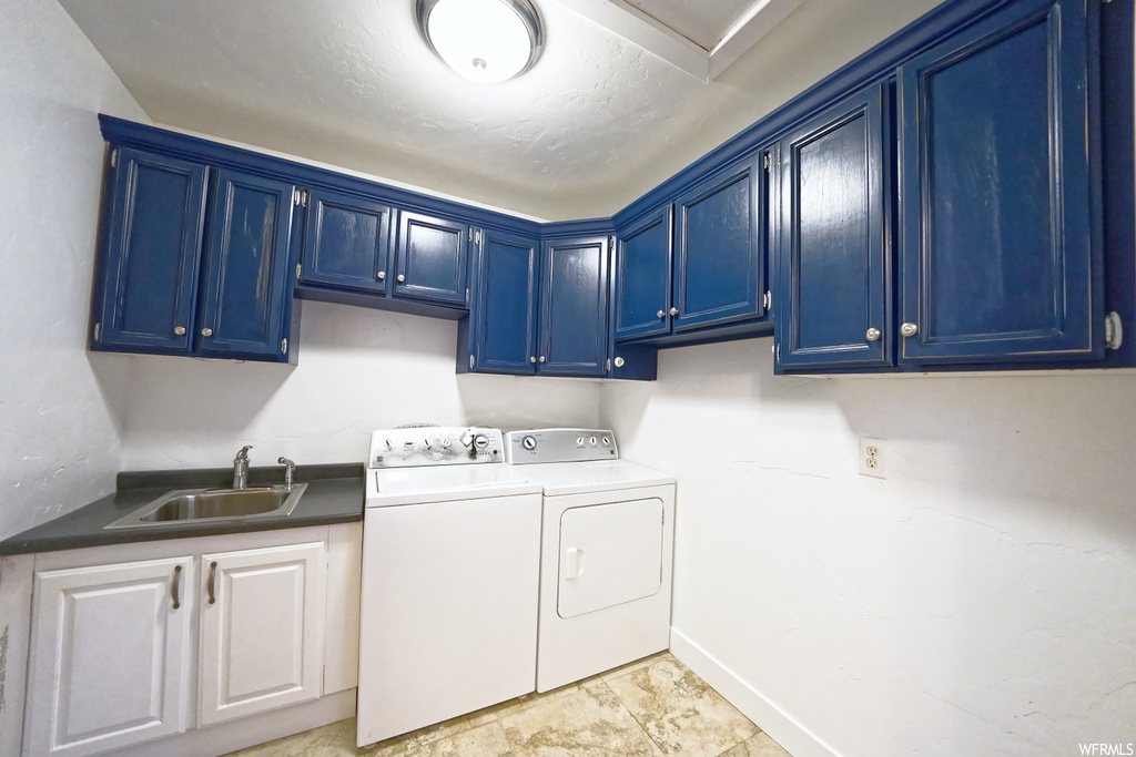 Washroom with cabinets, washing machine and clothes dryer, sink, and light tile flooring