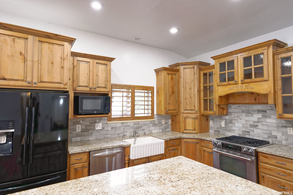 Kitchen with premium range hood, sink, light stone countertops, tasteful backsplash, and black appliances
