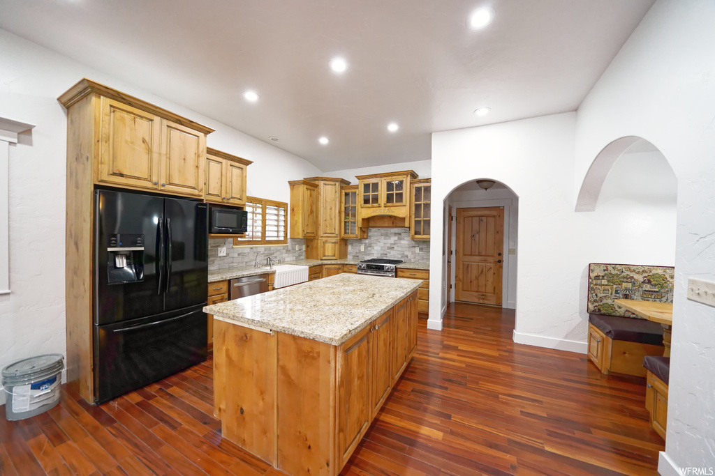 Kitchen featuring light stone countertops, backsplash, dark hardwood / wood-style floors, black appliances, and a kitchen island
