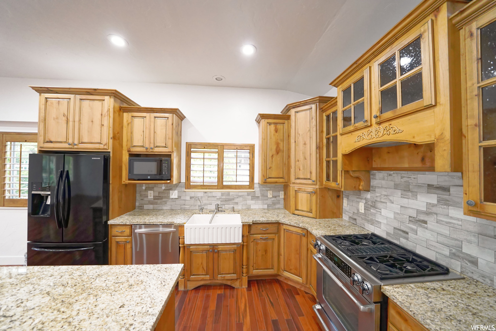 Kitchen featuring sink, light stone counters, dark hardwood / wood-style flooring, backsplash, and black appliances