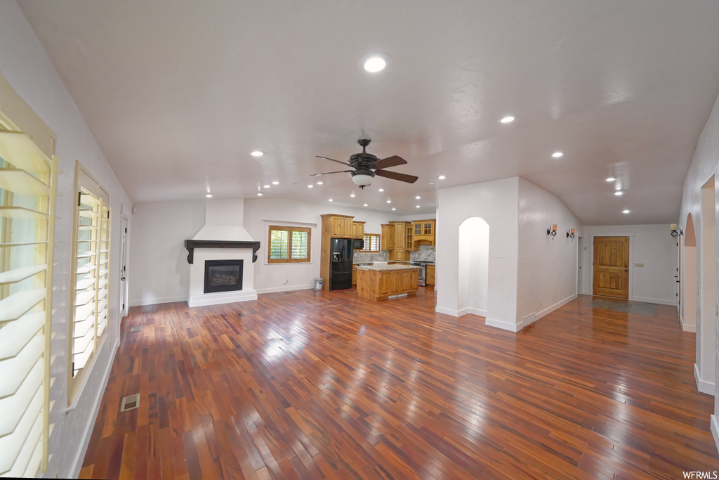 Unfurnished living room featuring dark hardwood / wood-style flooring, ceiling fan, and vaulted ceiling