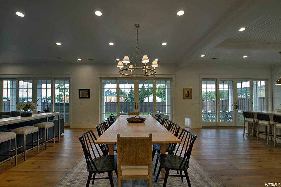 Wood floored dining room featuring a chandelier, french doors, plenty of natural light, and beamed ceiling