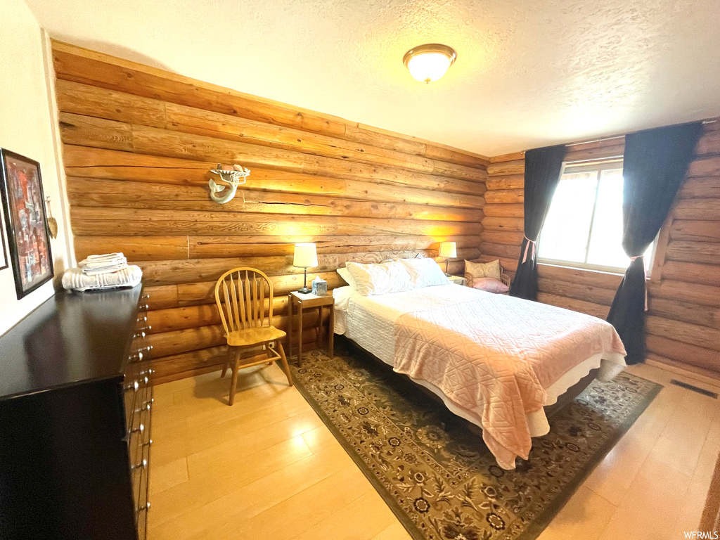 Hardwood floored bedroom featuring log walls and a textured ceiling