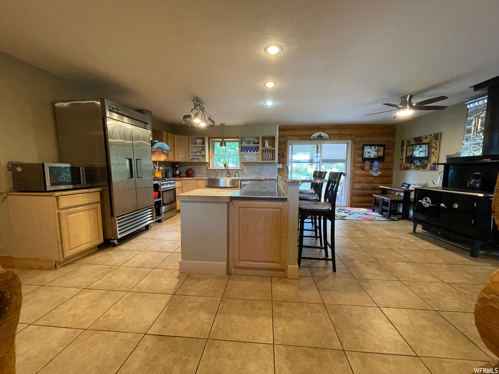 Kitchen featuring backsplash, a kitchen island, light tile floors, ceiling fan, and stainless steel range