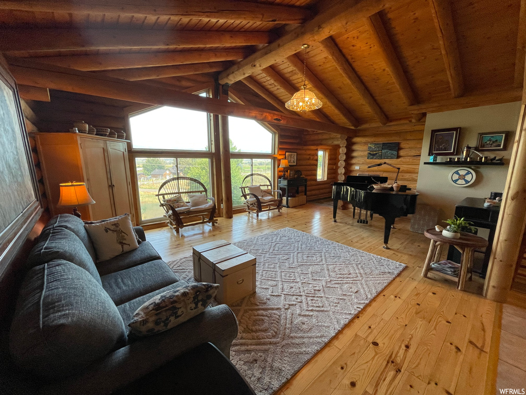 Living room with log walls, lofted ceiling with beams, wooden ceiling, and light hardwood flooring