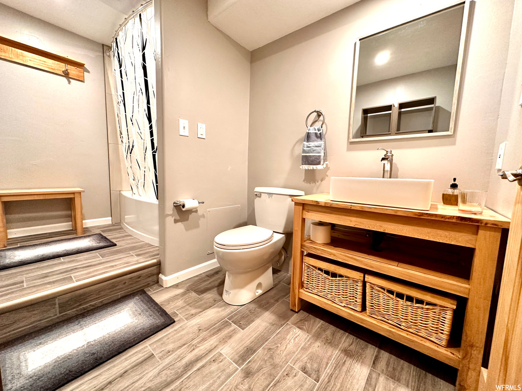 Full bathroom with light hardwood flooring, shower / tub combo with curtain, mirror, and vanity