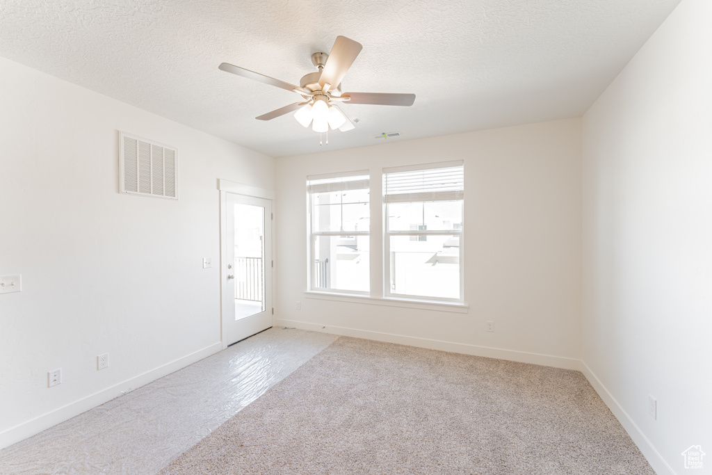 Empty room featuring light colored carpet, a textured ceiling, and ceiling fan