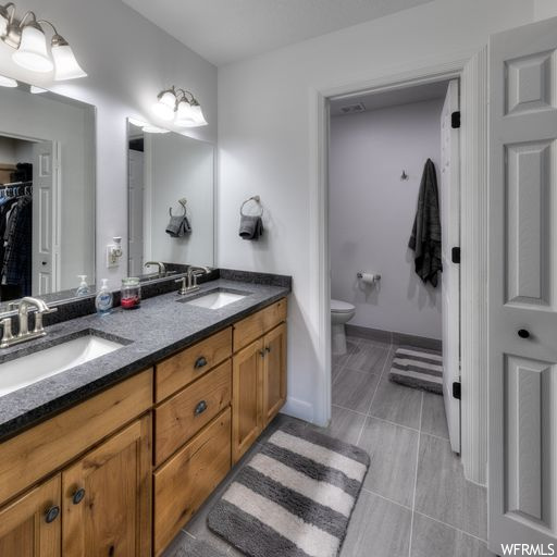 Bathroom with dual vanity, mirror, and light tile floors