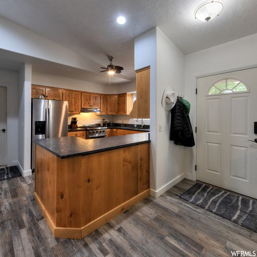 Kitchen with range, brown cabinets, ceiling fan, dark hardwood flooring, dark countertops, and stainless steel fridge with ice dispenser