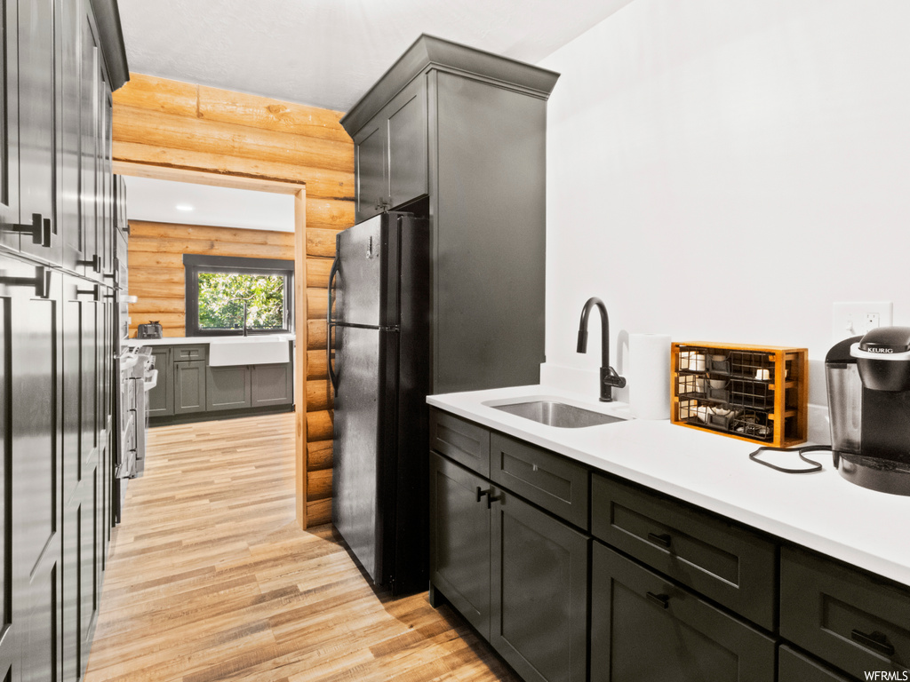 Interior space with log walls, light countertops, light hardwood flooring, black fridge, and dark brown cabinetry